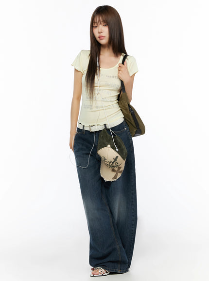 Cruz Wide Leg Jeans IL523 Dark blue full-body front view on model, styled with yellow graphic tee, white belt, olive shoulder bag, cap in hand, looking down