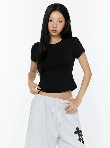 Curved Hem Baby Tee IL516 Black front shot on model pulling hem, showing fitted stretch fabric and cropped cut with curved hem detail