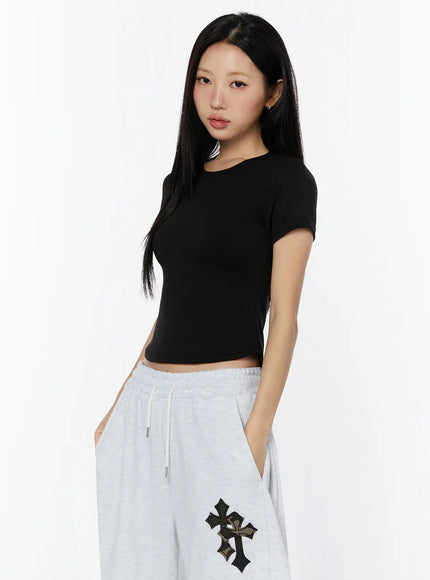 Curved Hem Baby Tee IL516 Black side shot on model showing fitted silhouette, ribbed knit texture detail at hem, hand holding fabric edge