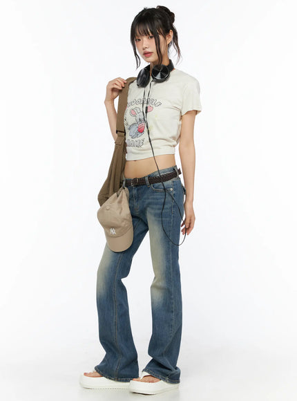 Dawn Low Rise Bootcut Jeans CU530 Blue full-body side-angle shot on model styled with graphic crop tee, cap, headphones and canvas shoulder bag
