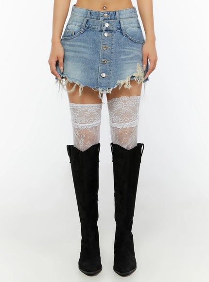 Distressed Mini Denim Skirt IL524 Blue front waist-down shot on model showing button-fly, frayed hem, and white lace thigh-high socks with black over-the-knee boots
