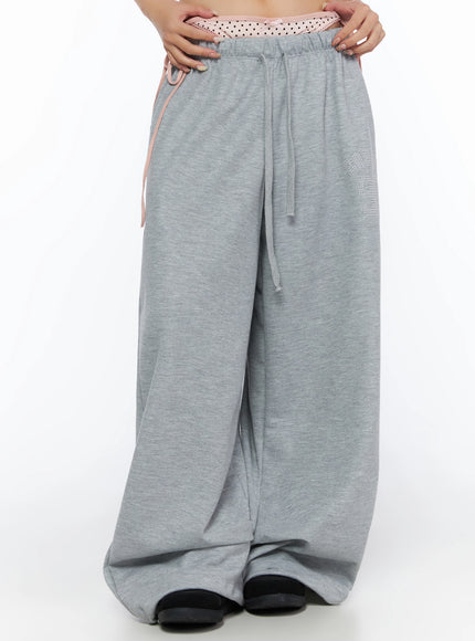 Dot Print Sagging Sweatpants IL515 Gray front cropped shot on model hands at waistband showing pink polka dot layered panel drawstring and rhinestone logo