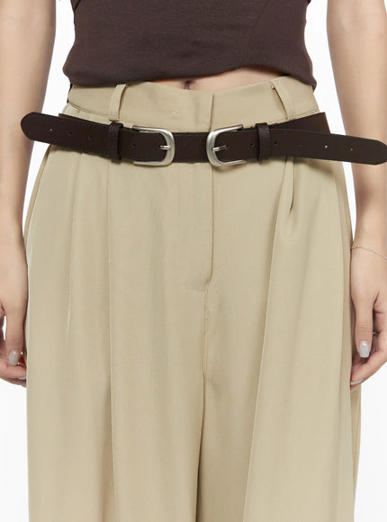 Double Buckle Faux Leather Belt CL527 Brown detail close-up on model showing dual silver buckles worn over beige pleated wide-leg pants