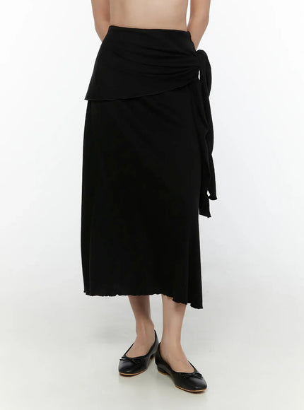 Draped Wrap Maxi Skirt CL520 Black front shot on model showing layered wrap panel, side tie, pleated maxi length, and ballet flats