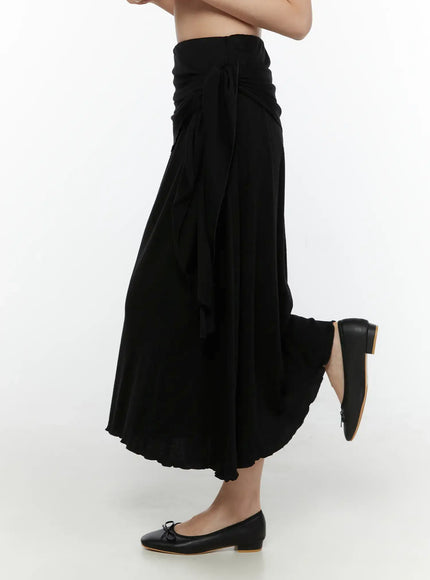 Draped Wrap Maxi Skirt CL520 Black side shot on model showing full skirt length, flared hem, and side tie detail with ballet flats