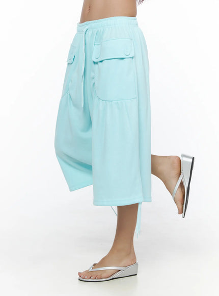 Drawstring Bermuda Shorts CL513 Mint side shot on model with leg raised showing wide-leg silhouette, curved patch pockets, and drawstring hem ties with silver sandals
