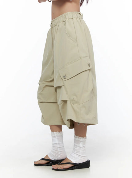 Drawstring Cargo Jorts CL510 Beige angled side shot on model showing cargo pocket flap with snap buttons, tiered drape, and black wedge flip-flop sandals