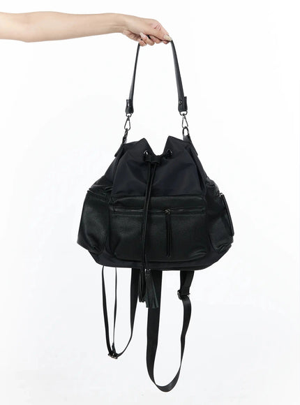 LEWKIN Drawstring Pocket Bucket Bag IL515 Black hand-held shot showing front zip pockets, nylon body, pebbled leather panels, tassel drawstring, and backpack straps