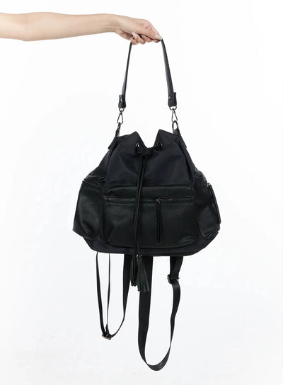 LEWKIN Drawstring Pocket Bucket Bag IL515 Black hand-held shot showing front zip pockets, nylon body, pebbled leather panels, tassel drawstring, and backpack straps