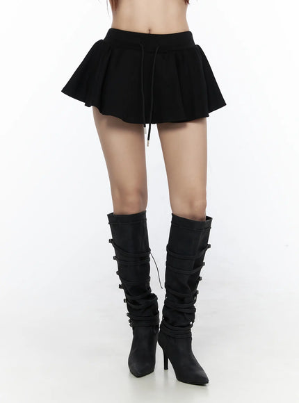 LEWKIN Elastic Waist Tiered Ruffle Mini Skirt CL524 Black S/M front close-up on model, flared pleated skirt with drawstring waist and metal aglets, paired with black buckle knee-high heeled boots