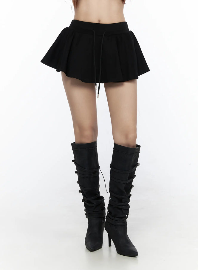 LEWKIN Elastic Waist Tiered Ruffle Mini Skirt CL524 Black S/M front close-up on model, flared pleated skirt with drawstring waist and metal aglets, paired with black buckle knee-high heeled boots