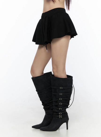 Elastic Waist Tiered Ruffle Mini Skirt CL524 Black side-view close-up on model, showing flared tiered silhouette, elastic waistband, and drawstring with metal tips, styled with buckle boots