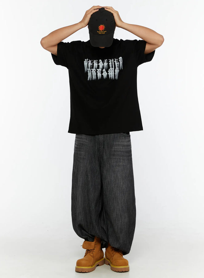 LEWKIN Embroidered Sun Logo Cap IL515 Black One Size front view on model styled with oversized graphic tee and wide-leg denim, hands raised on head