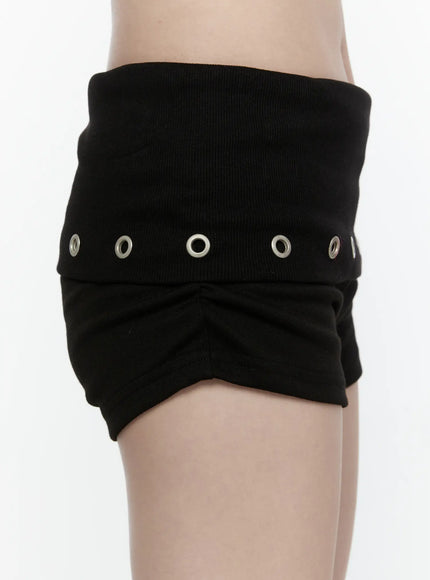Eyelet Detail Mini Shorts IL522 Black side close-up on model showing ribbed fold-over waistband, silver grommet detail, and gathered fabric texture