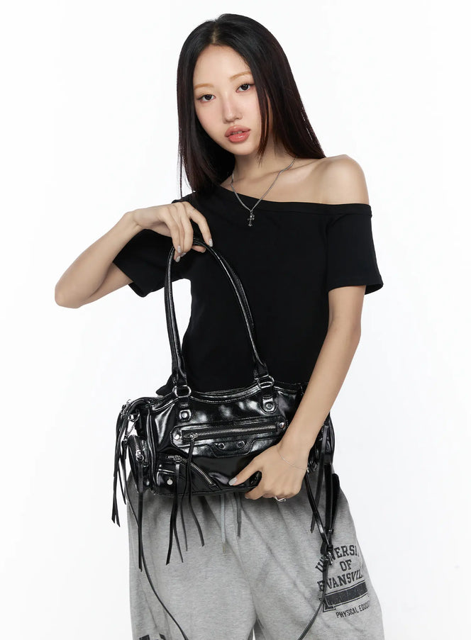 Faux Leather Shoulder Bag CL527 Black front view on model hand-carrying with dual top handles, glossy faux leather with silver zipper pockets and fringe tassels, styled with black off-shoulder top
