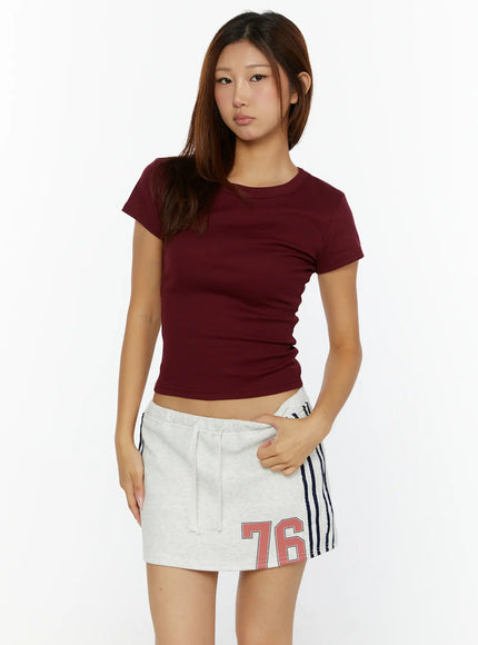 Fitted Crop Top CL515 burgundy front view on model standing with hand in skirt pocket showing crew neck and slim crop fit