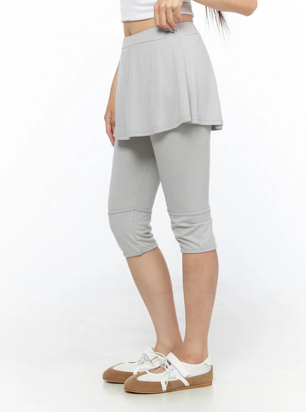 Flare Skort CL517 Light gray side view on model standing, hand at waistband showing elastic waist detail, flared skirt overlay above capri leggings, white sneakers