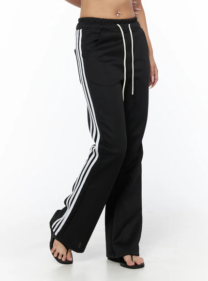Flared Striped Track Pants CU524 Black front close-up on model showing elastic waistband with cream drawstring and triple white side stripes