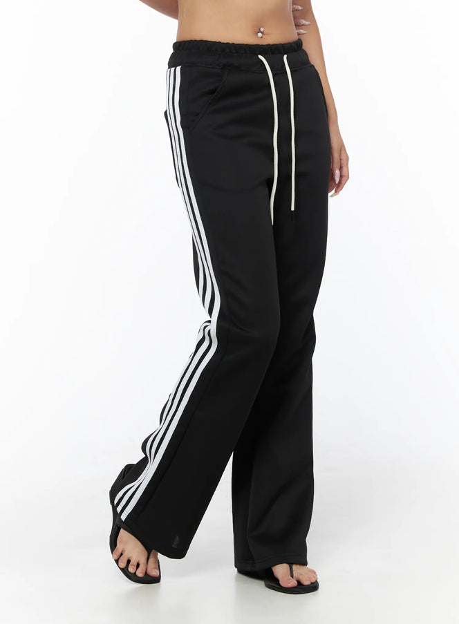 Flared Striped Track Pants CU524 Black front close-up on model showing elastic waistband with cream drawstring and triple white side stripes