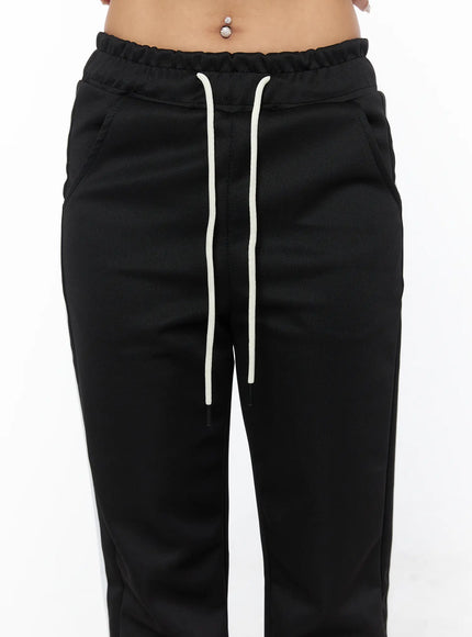Flared Striped Track Pants CU524 Black close-up detail of elastic waistband with cream drawstring and side pocket on model