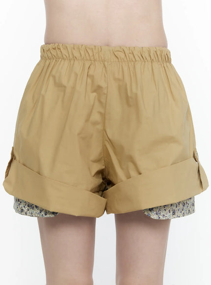Floral Banded Shorts IL521 Beige side full-length shot on model in plaid crop shirt and loafers, touching cuffed hem with floral layer
