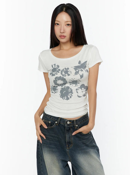 Floral Graphic Round-Shoulder Top CU529 White cropped front shot on model with hands in pockets, gray multi-floral butterfly graphic, scoop neck, slim ribbed short-sleeve top
