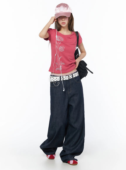 Floral Graphic Short Sleeve Top IU525 Dark pink full-body front shot model adjusting pink satin cap styled with earphones crossbody bag star belt wide-leg jeans