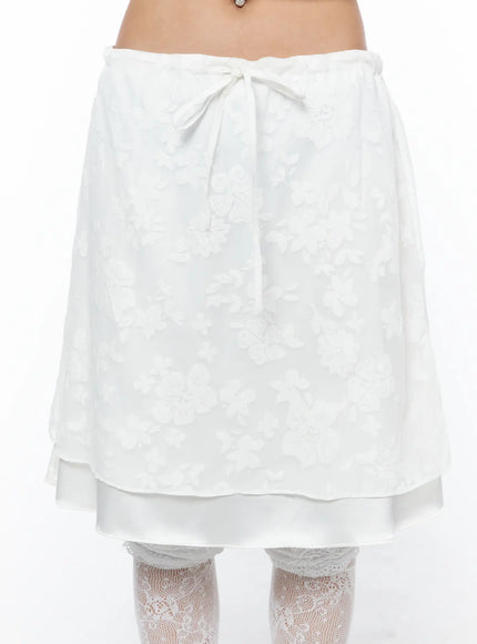Floral Midi Skirt CU523 White close-up front shot on model highlighting tonal floral jacquard fabric, center bow tie waist, and layered hem detail