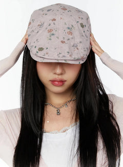 LEWKIN Floral Print Flat Cap IU524 Pink front model shot with both hands lifting brim over eyes, ditsy rose print, styled with lace top