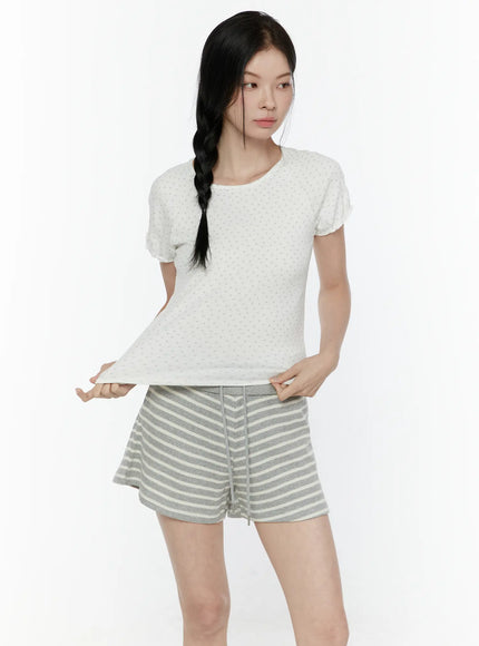 Floral Puff Short Sleeve Top IL506 White front view on model lifting hem to show crop length and fabric texture with gray striped shorts