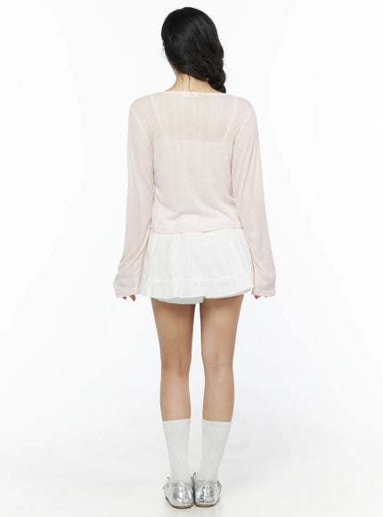 Flower Button Ribbed Cardigan IU525 Light pink back model shot showing ribbed knit texture cropped hem and long sleeves with flared cuffs over white pleated mini skirt