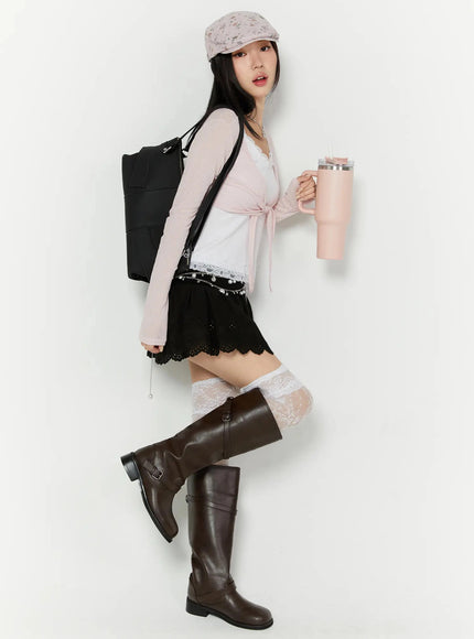 Foldover Eyelet Lace Mini Skirt IU524 Black side full-body lifestyle shot on model walking with backpack and tumbler styled with pink cardigan lace socks and tall boots