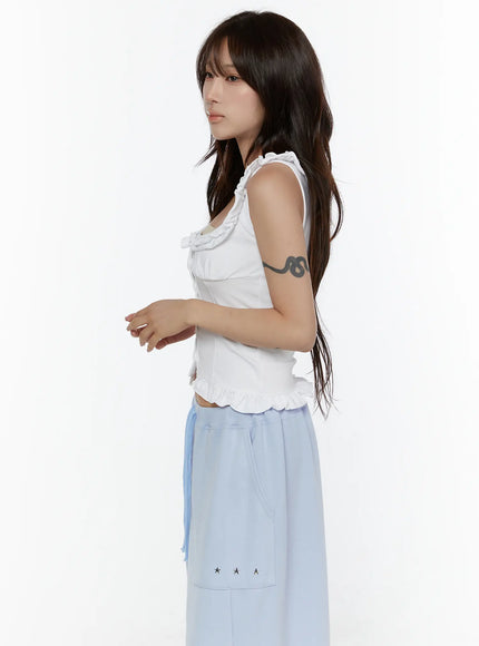 Frill Button Sleeveless Top CL507 White side view on model showing fitted corset silhouette, ruffled shoulder strap and scalloped hem with light blue pants