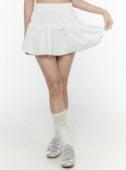 Frill Tiered Mini Skirt IL506 White front detail shot on model lifting skirt hem to reveal double ruffle tiers, light woven fabric texture