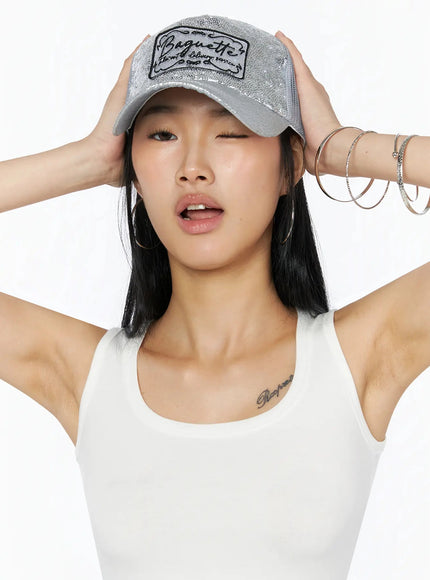 LEWKIN Glitter Patch Trucker Cap IL509 Silver close-up front on model hands raised holding brim sequin texture and Baguette embroidered patch detail