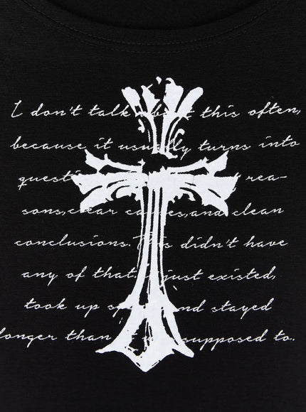 Gothic Cross Slim Fit Top IU525 Black close-up flat detail shot, white gothic ornate cross and white cursive script print contrast on black fabric, scoop neckline visible