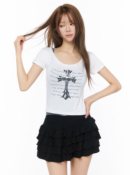 Gothic Cross Slim Fit Top IU525 White front model shot, hair-tossing dynamic pose, gothic cross print, slim fit crop length, layered over grey inner, black ruffle skirt