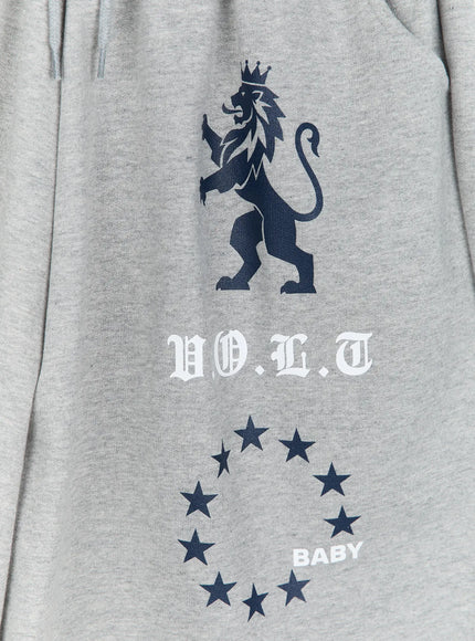 Graphic Bermuda Shorts CL524 Grey close-up detail of navy crowned lion, V.O.L.T old-English text and BABY star circle print on grey fabric