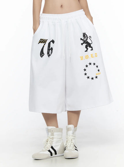 Graphic Bermuda Shorts CL524 White front close-up on model showing 76 star flag, crowned lion, V.O.L.T and BABY star circle prints with drawstring waist