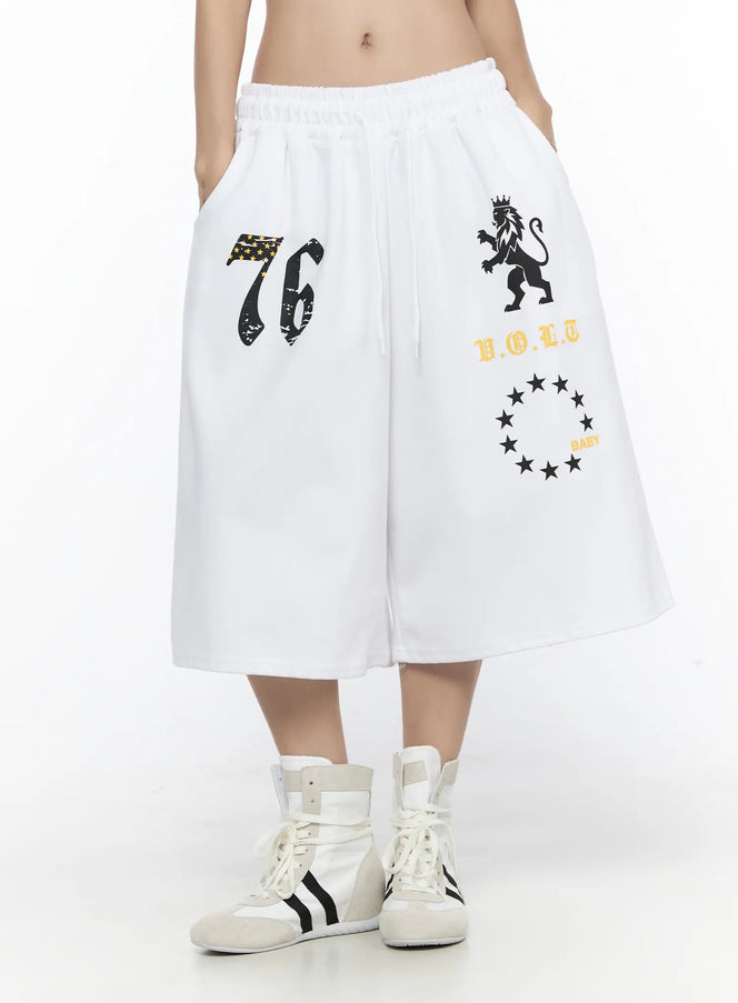 Graphic Bermuda Shorts CL524 White front close-up on model showing 76 star flag, crowned lion, V.O.L.T and BABY star circle prints with drawstring waist