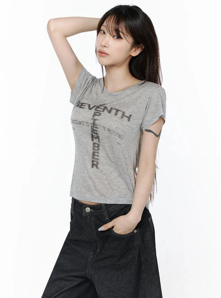 Graphic Casual Tee IL502 Gray side-angle shot model one hand on head semi-sheer crop tee cross graphic print styled with black wide-leg jeans edgy pose