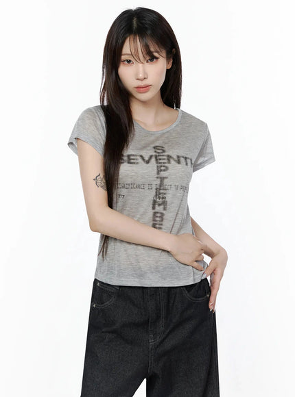 Graphic Casual Tee IL502 Gray front shot model slight angle arms at sides semi-sheer crop tee with cross graphic print round neck short sleeves with dark jeans