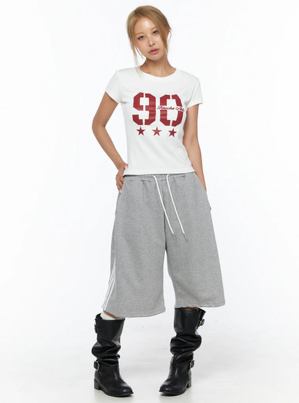 Graphic Crop Tee CU523 White front full-body shot on model standing straight, red 90 Fousche Arts graphic, cropped hem, styled with gray wide-leg pants and black boots