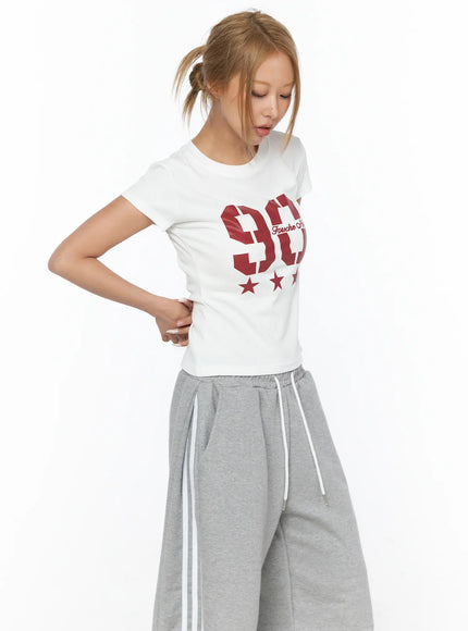 Graphic Crop Tee CU523 White S/M side-angle shot on model with ponytail, red 90 star graphic print, slim cotton crop fit, styled with gray wide-leg sweatpants