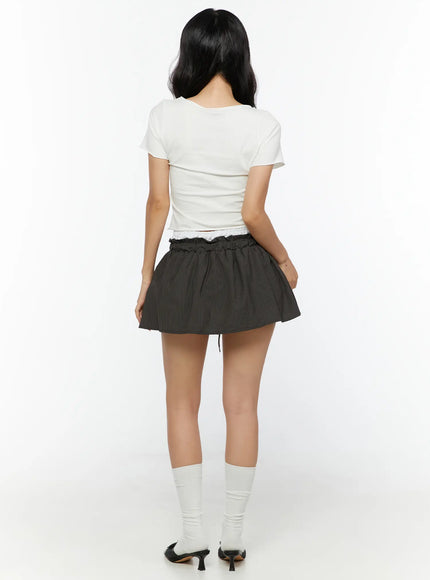 Graphic Cropped Tee CU526 White back model shot revealing plain back, short sleeves, cropped hemline, paired with dark pinstripe mini skirt and heels