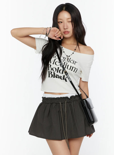 LEWKIN Graphic Cropped Tee CU526 White M/L front model shot off-shoulder styled with black graphic print, accessorized with crossbody bag and layered necklaces