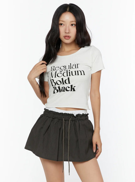 Graphic Cropped Tee CU526 White three-quarter front model shot with hand in hair, showing full typography graphic print and cropped ribbed fit