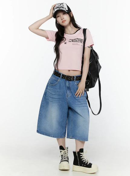 Graphic Cropped Tee IL521 Light pink front view on model with cap and black backpack, hand on cap brim, full-body styling with wide denim shorts and platform sneakers