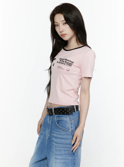 Graphic Cropped Tee IL521 Light pink three-quarter side view on model gazing forward, black ringer collar, Midnight Structure graphic print visible, paired with wide-leg jeans