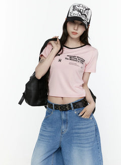 LEWKIN Graphic Cropped Tee IL521 Light pink S/M front view on model wearing cap and backpack, black ringer neckline, archive graphic print, styled with wide-leg jeans